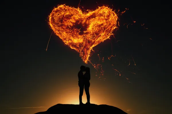 Paar auf einem Hügel im Dunkeln, darüber ein feuriges Herz, erstellt aus Feuer-Texturen.